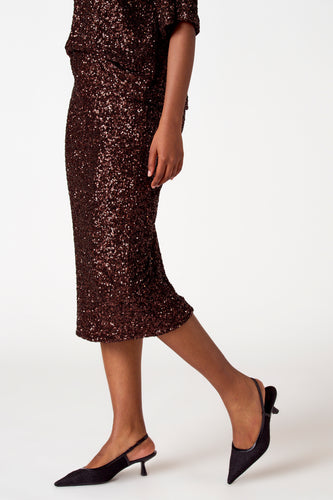 Bruine paillettenjurk met zwarte pumps.
