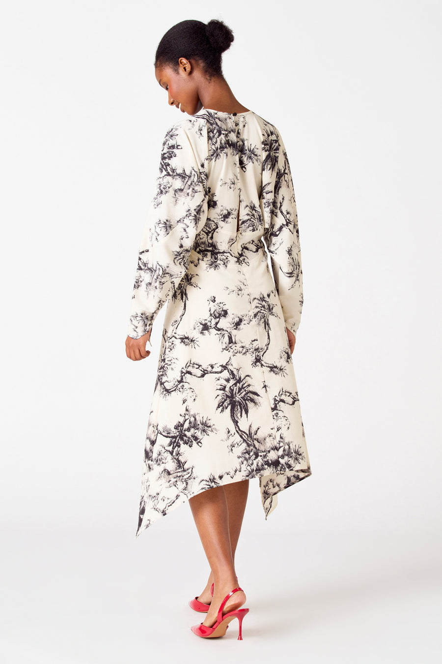 Vrouw in jurk met palmbomenprint en rode hakken.