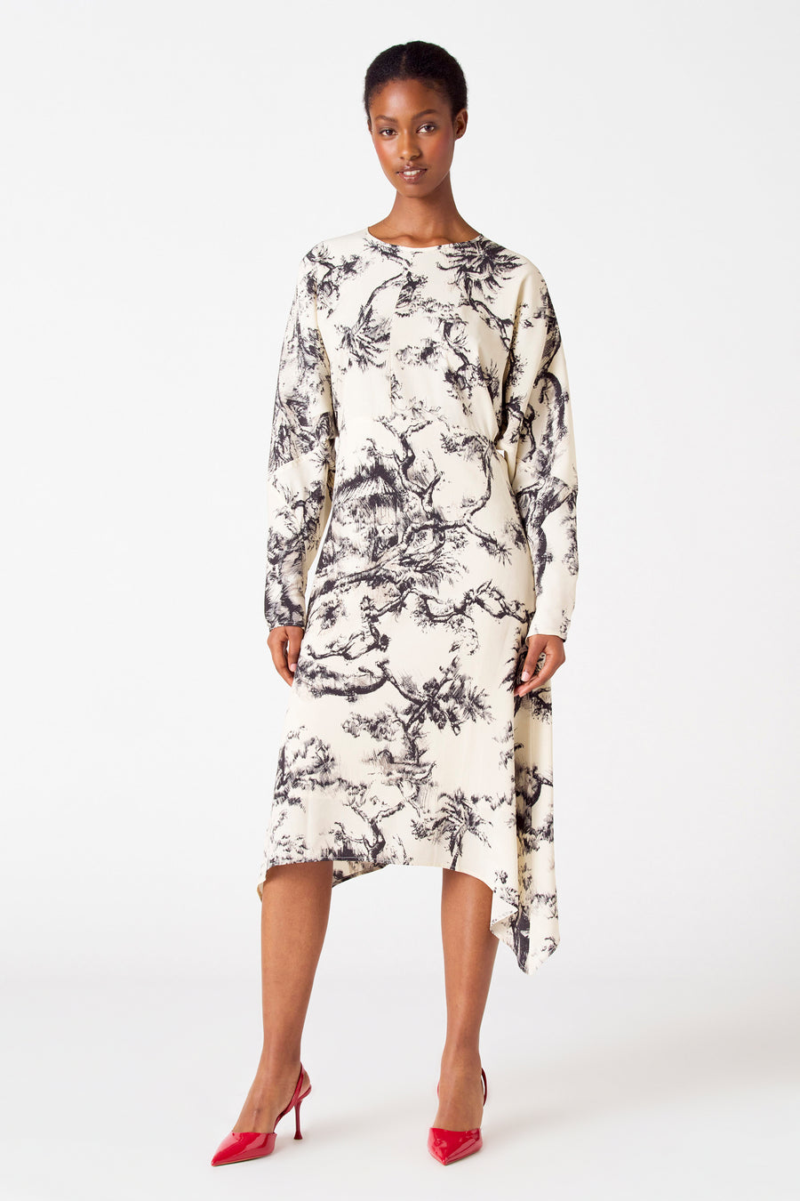 Vrouw in crèmekleurige jurk met zwarte print en rode hakken, staand.