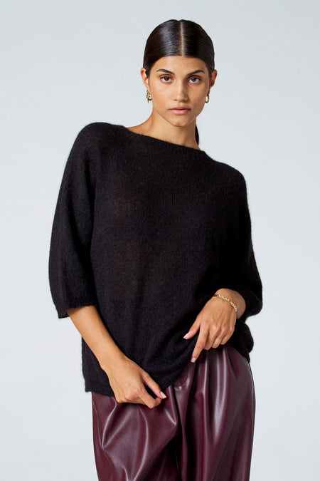 Pull noir avec col rond d'Astrid Black Label, porté avec un pantalon de cuir bordeaux et une bague en or, en vue latérale.