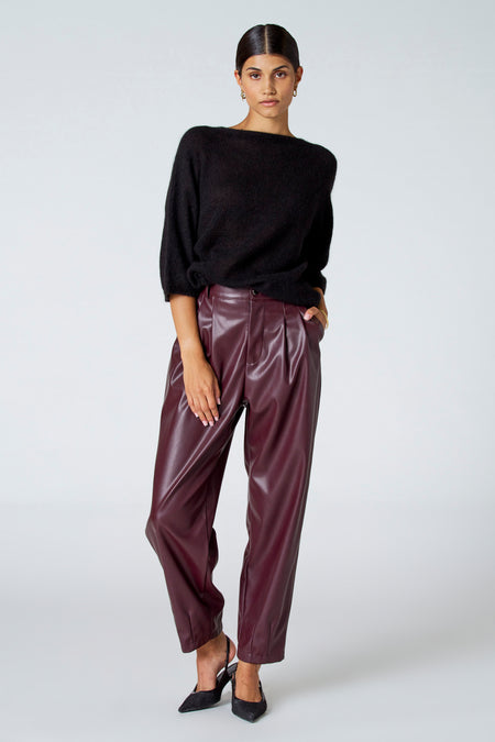 Pull noir avec col rond d'Astrid Black Label, associé à un pantalon en cuir bordeaux et des bottes noires.