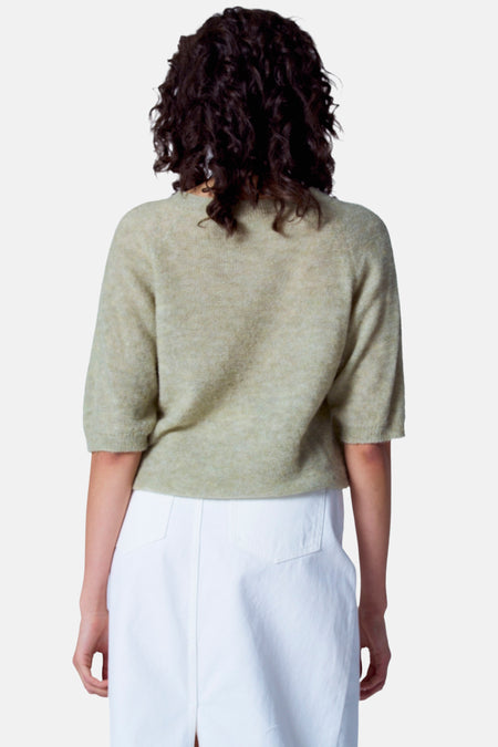T-shirt vert avec col rond d'Astrid Black Label, à manches courtes et porté avec une jupe blanche.