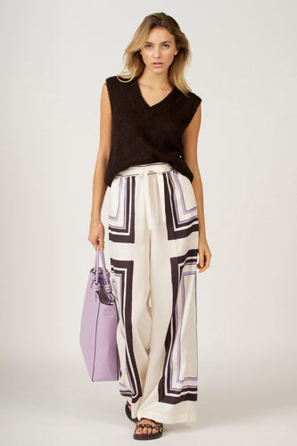 Vrouw in zwarte trui, gebloemde broek en paarse tas.