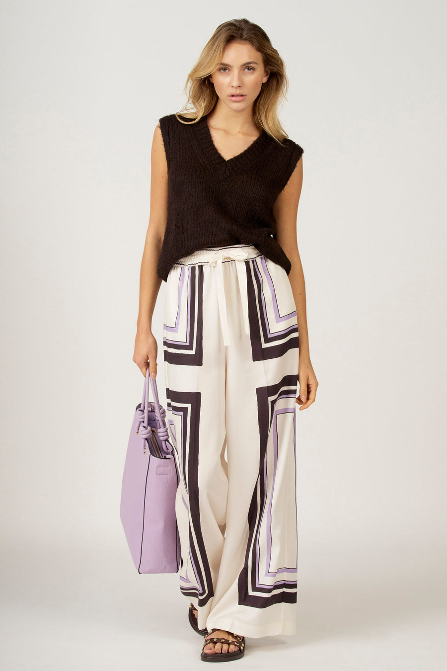 Vrouw in zwarte trui, gebloemde broek en paarse tas.