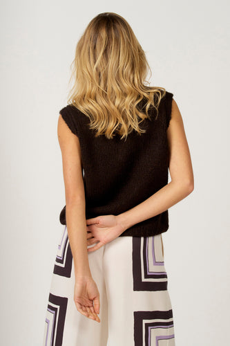 Achterkant van een vrouw in een bruin gebreid vest en een broek met geometrisch patroon.