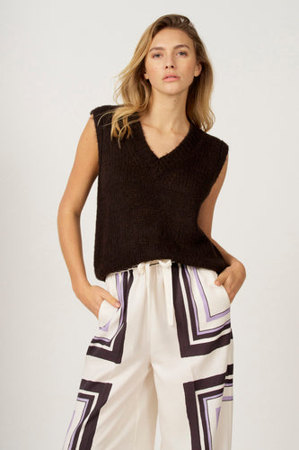 Model met een mouwloze trui en broek met geometrisch patroon.