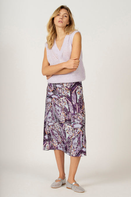 Vrouw in lila vest en paarse rok, gekruiste armen, zilveren schoenen.