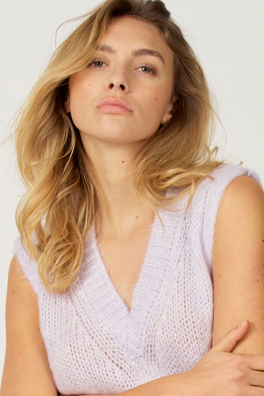 Blonde vrouw draagt lila gebreide mouwloze top, lichte achtergrond.