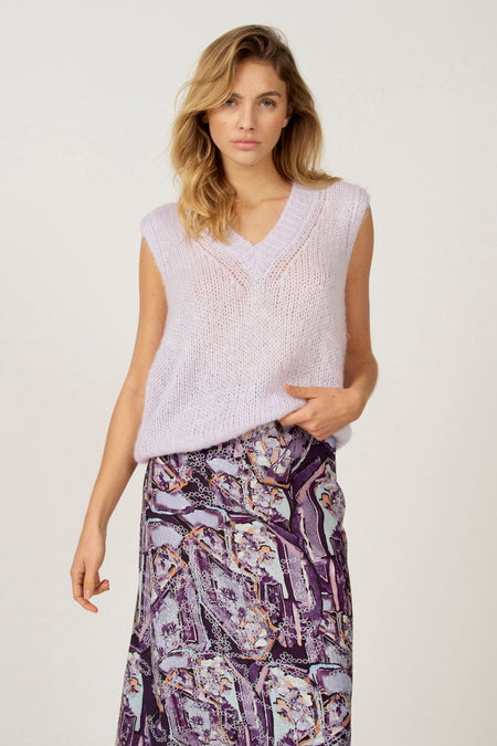 Vrouw met blonde haren draagt lila gebreide top en paarse rok.