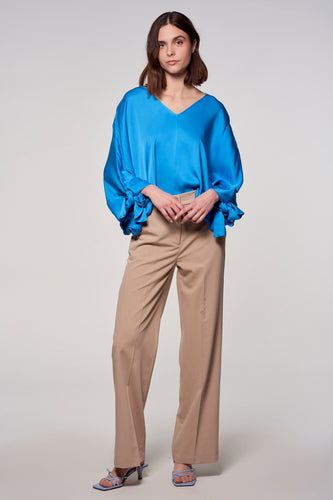 Vrouw met blauwe blouse en beige pantalon.