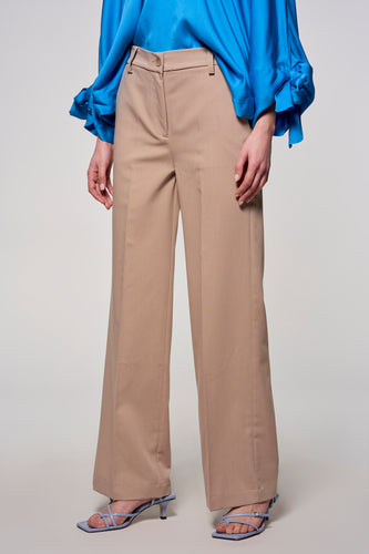 Een persoon die een blauwe blouse en beige, wijde pantalon draagt, met blauwe hakken.