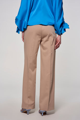 Achterkant van een model met een blauwe blouse en een beige pantalon.