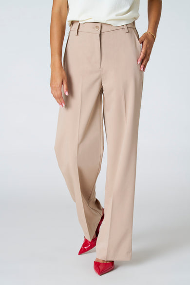 Pantalon beige d'Astrid Black Label, avec des jambes larges et des chaussures rouges.