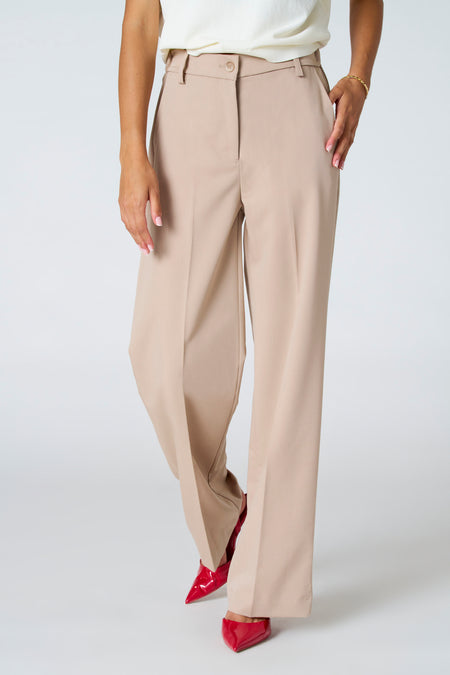 Pantalon beige d'Astrid Black Label, avec des jambes larges et des chaussures rouges.