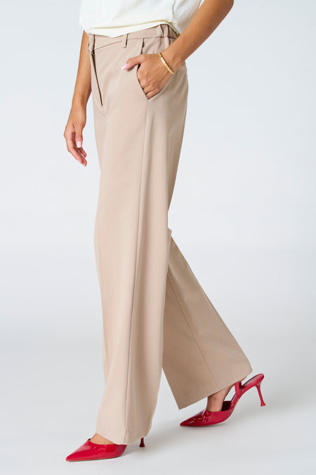 Pantalon beige d'Astrid Black Label, avec poche latérale et talons rouges.