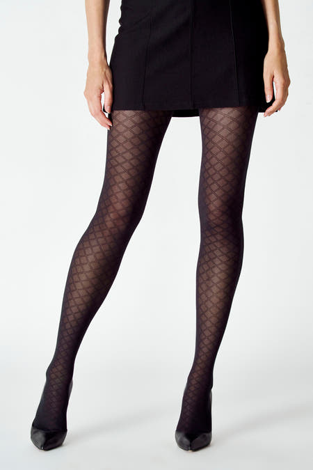 Pantys noirs d'Astrid Black Label avec motif de carreaux, portés avec une mini-jupe noire et des talons assortis sur un fond blanc.