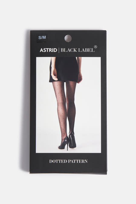 Pantys noirs d'Astrid Black Label avec un motif à points, portés avec une jupe noire et des bottes noires.