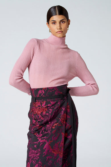 Roze ribbeltrui met rolkraag van Astrid Black Label, strak model, gedragen met een bloemenrok en gouden oorbellen, front view
