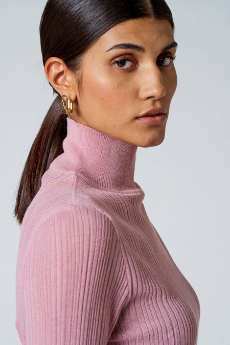 Roze rolkraagtrui van Astrid Black Label, ribbelstructuur, zijdelingse close-up, model met gouden oorbellen
