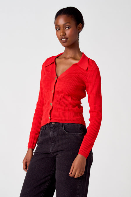 Gilet rouge d'Astrid Black Label, avec une texture finement rayée et une fermeture à boutons dorés, porté avec un jean foncé.