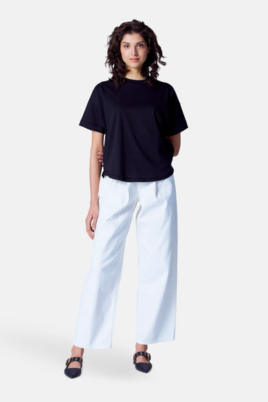 T-shirt noir à manches courtes d'Astrid Black Label, porté avec un short blanc et des chaussures noires à boucles.