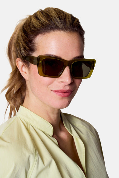 Lunettes de soleil vertes d'Astrid Black Label, portées par une femme avec une chemise claire et des cheveux relevés.