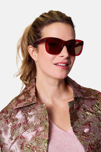 Lunettes de soleil roses d'Astrid Black Label, portées par une femme avec un manteau rose à motif brocart.