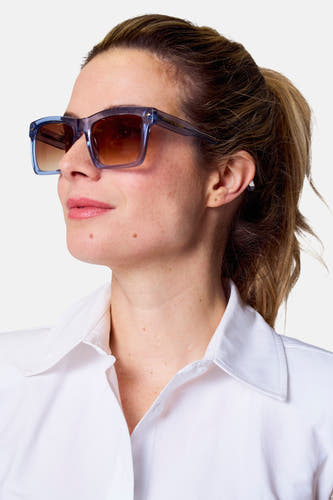 Lunettes de soleil bleues d'Astrid Black Label, portées par une femme avec un chemisier blanc et une queue de cheval.