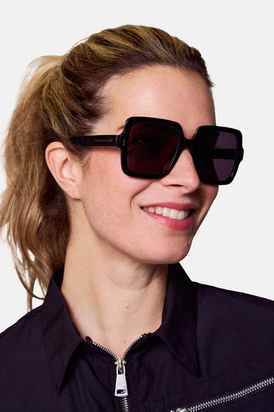 Lunettes de soleil noires d'Astrid Black Label, portées par une femme en une chemise noire avec une fermeture éclair argentée.