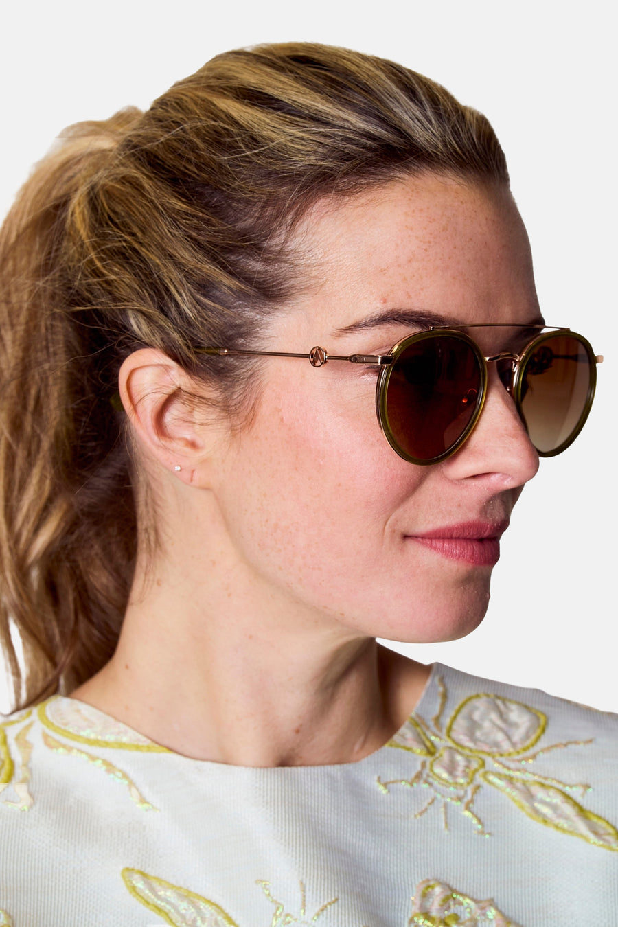 Lunettes de soleil roses d'Astrid Black Label, avec un cadre doré et des verres marrons, portées par une femme en profil latéral.