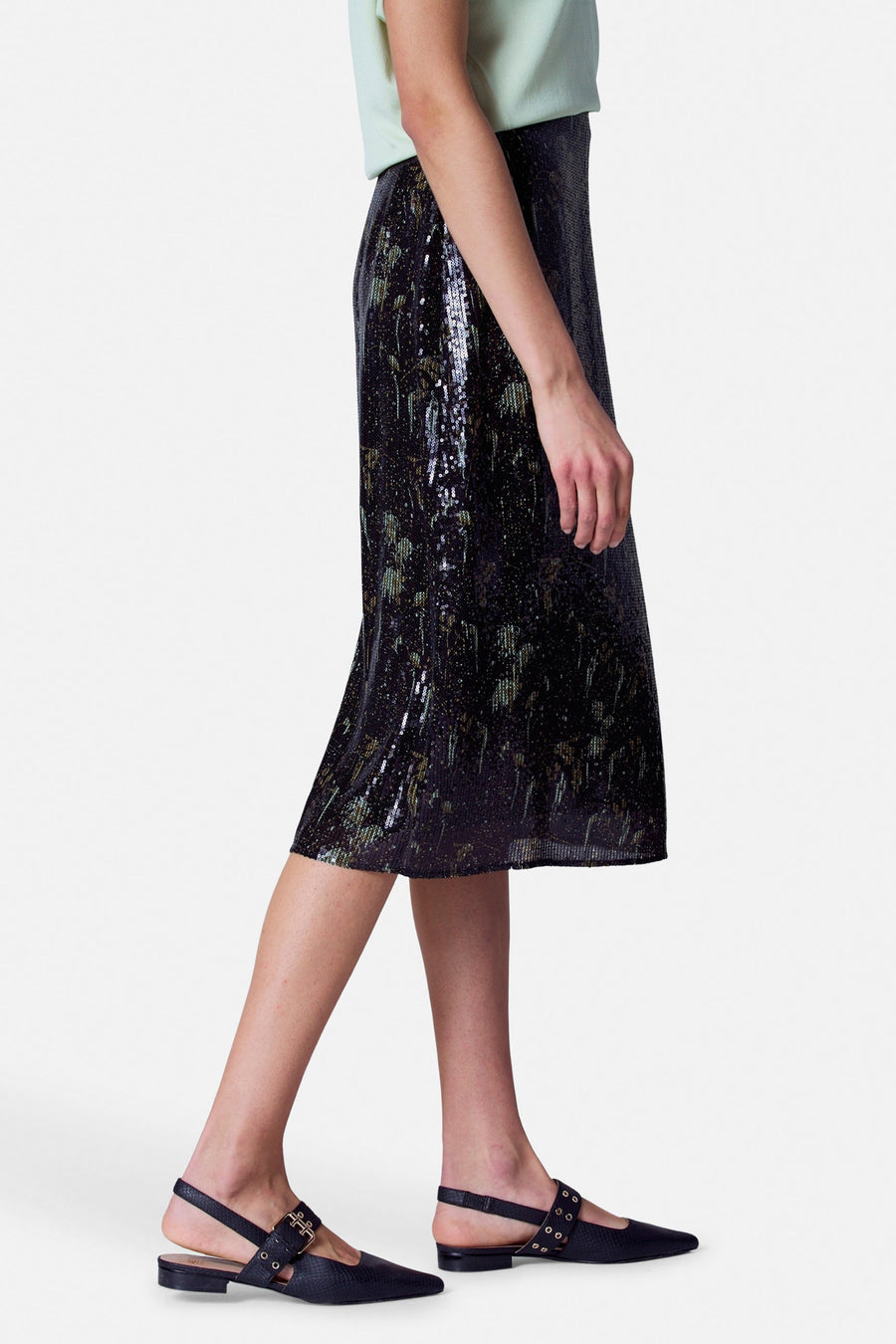 Robe noire Astrid Black Label, avec paillettes et une longueur midi, portée avec un haut vert clair et des sandales à brides noires.