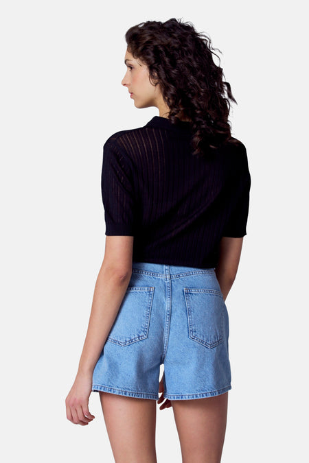 Polo noir à manches courtes d'Astrid Black Label, avec une fine structure de lignes verticales, associé à des shorts en denim.