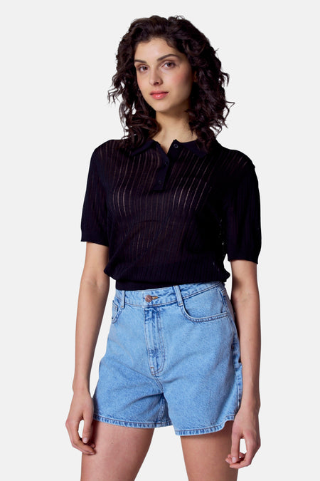 Polo noir à manches courtes d'Astrid Black Label, avec des boutons et porté avec des shorts en denim.