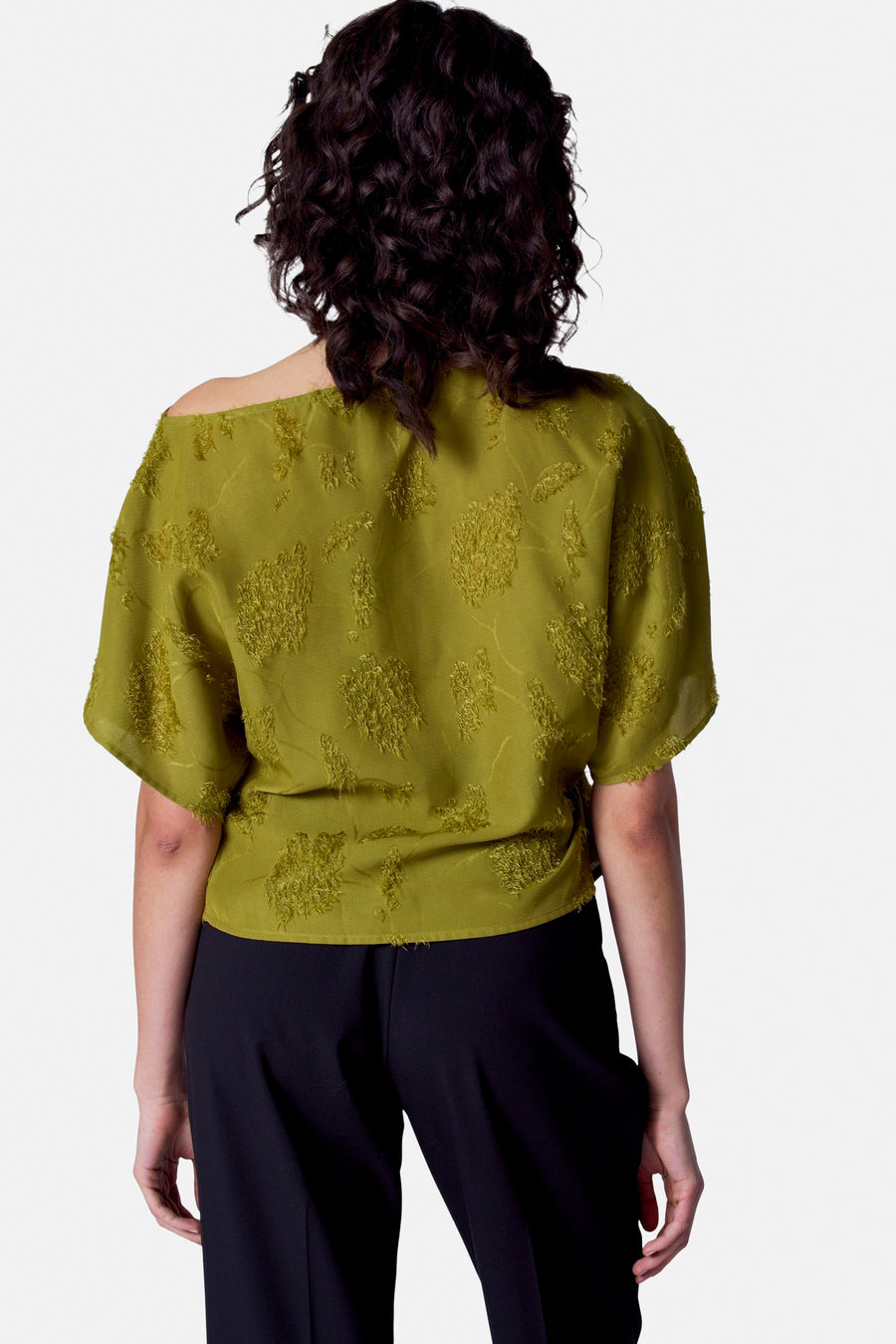 Achterkant van vrouw in olijfgroene blouse en zwarte broek.