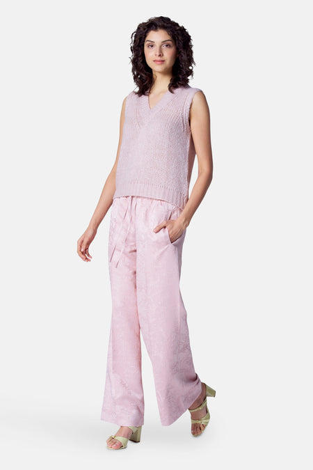 Pantalon rose d'Astrid Black Label avec un motif floral subtil et des jambes larges, associé à une chemise tricotée.