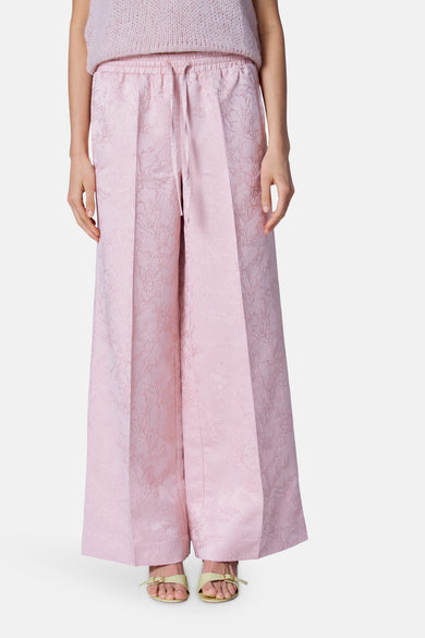Pantalon rose Astrid Black Label avec une texture subtile et des jambes larges, porté avec des sandales.
