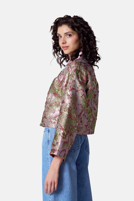 Manteau multicolore d'Astrid Black Label avec des motifs floraux dorés et verts, associé à un jeans bleu.