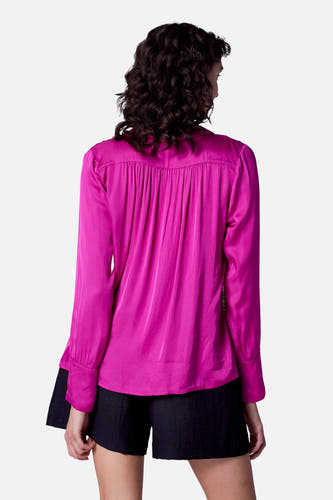Blouse rose à longues manches d'Astrid Black Label, avec des plis sur le dos, associée à une short noire.