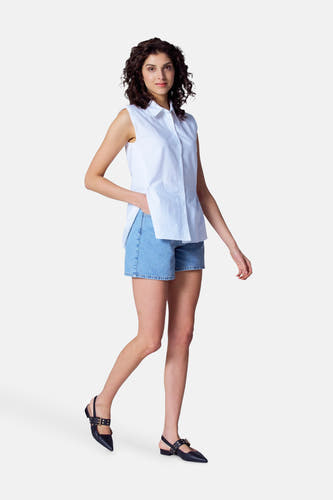 Blouse blanche à manches courtes d'Astrid Black Label, portée avec des shorts en denim et des sandales noires à brides.
