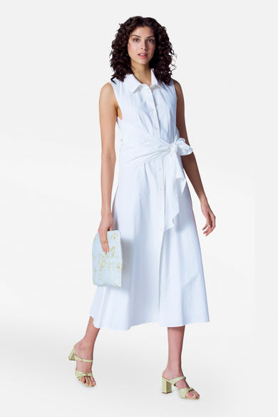 Robe sans manches d'Astrid Black Label, blanche avec détail de nœud et haut split, associée à un bracelet et des boucles d'oreilles dorés.
