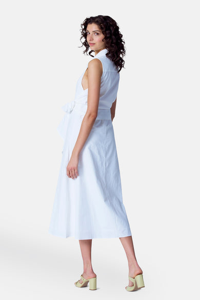 Robe blanche sans manches d'Astrid Black Label, avec une ceinture et un bas de jambe, portée avec des bottes claires.