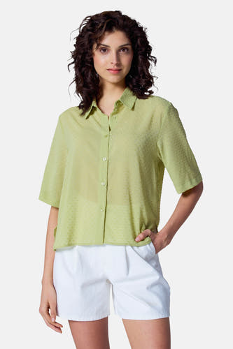 Blouse verte avec manches courtes d'Astrid Black Label, structurée et portée avec une short blanche.