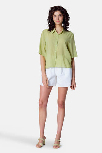 Blouse verte avec manches courtes d'Astrid Black Label, dotée d'un motif à carreaux subtil, associée à des shortts blancs et des talons.