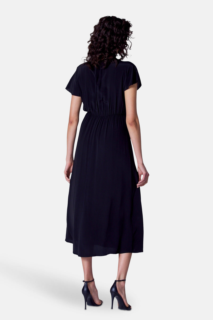 Zwarte kleedje met korte mouwen van Astrid Black Label, gezien van achteren, met elastische taille en zwarte hakken.
