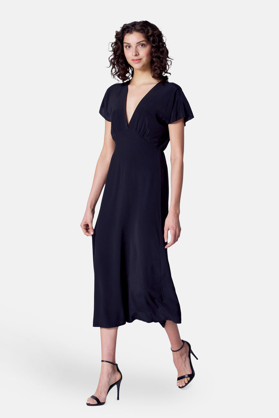 Robe noire à manches courtes d'Astrid Black Label, avec un col en V et des chaussures ouvertes à talons.