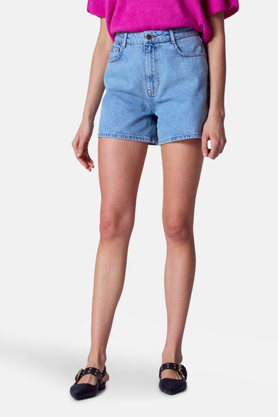 Short de denim bleu d'Astrid Black Label, porté avec un haut rose et des chaussures noires à boucles.