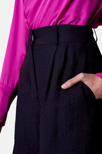 Short noir d'Astrid Black Label, avec une main dans la poche et une blouse magenta en soie.