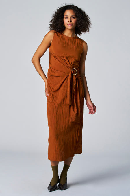 Robe sans manches brune Astridid Black Label, dr drapures, détails en tricots et etceau d'or, associée à des chaussettes vertes et des chaussures noires.