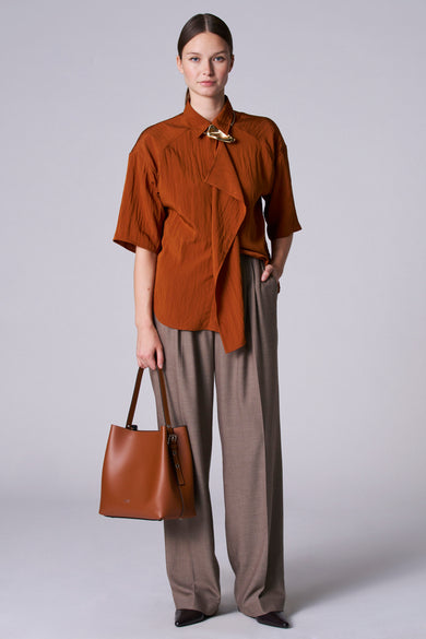 Blouse brune à manches trois-quarts d'Astrid Black Label, avec une fermeture décorative dorée et un détail drapé.