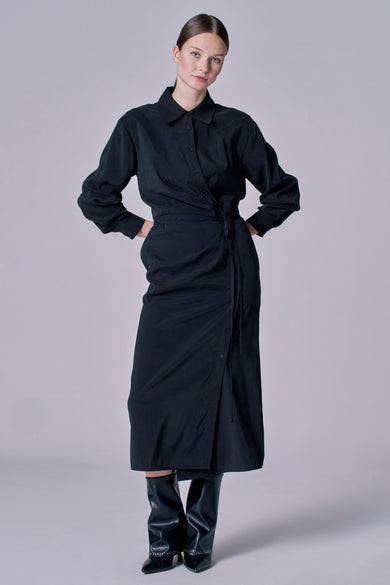 Zwarte kleedje met lange mouwen van Astrid Black Label, met overslagdetail en gedragen met zwarte laarzen.
